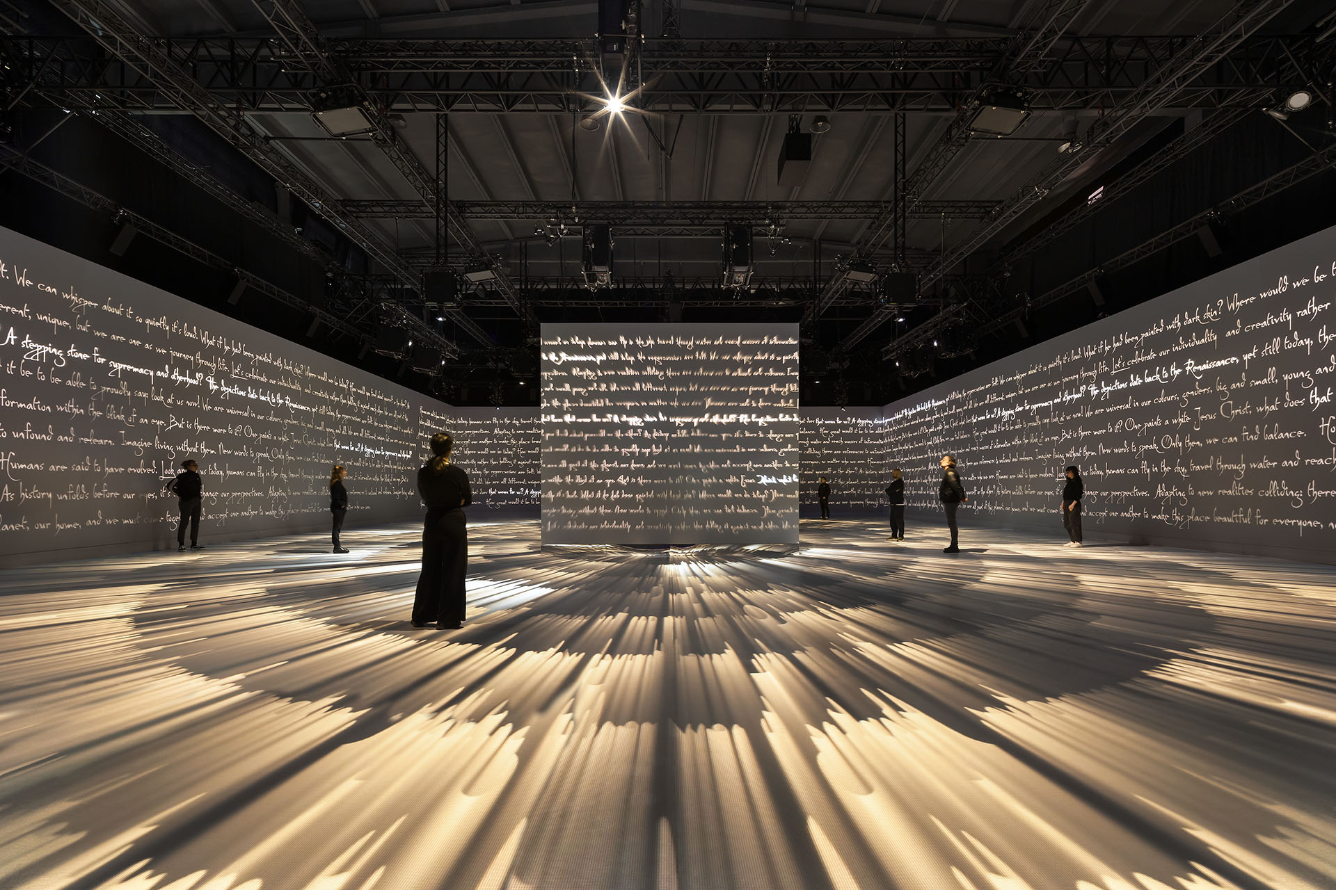 Visitors standing in a room wrapped with projected da Vinci handwriting